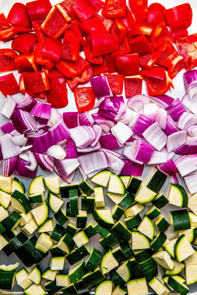 Chopped zucchini, red onion and red peppers on baking sheet before roasting.