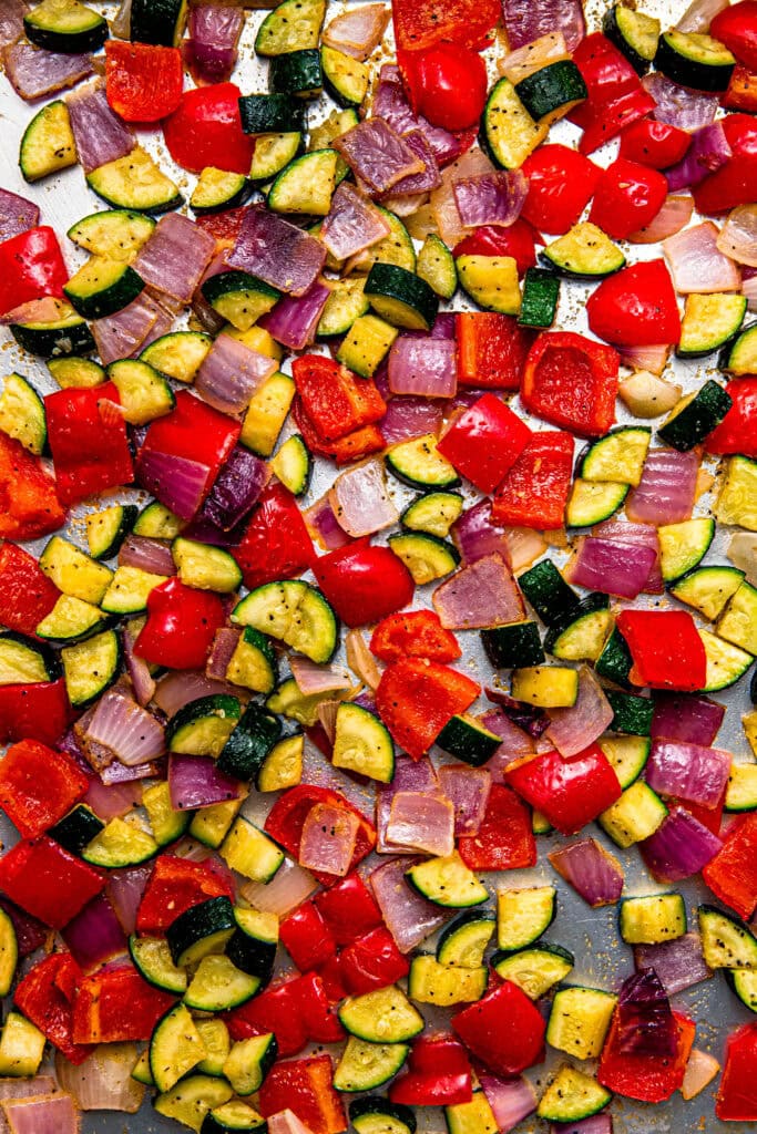 Finished roasted zucchini and red peppers on baking sheet after cooking in oven.