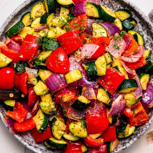 Overhead close up of serving plate of roasted zucchini and red peppers with red onion.