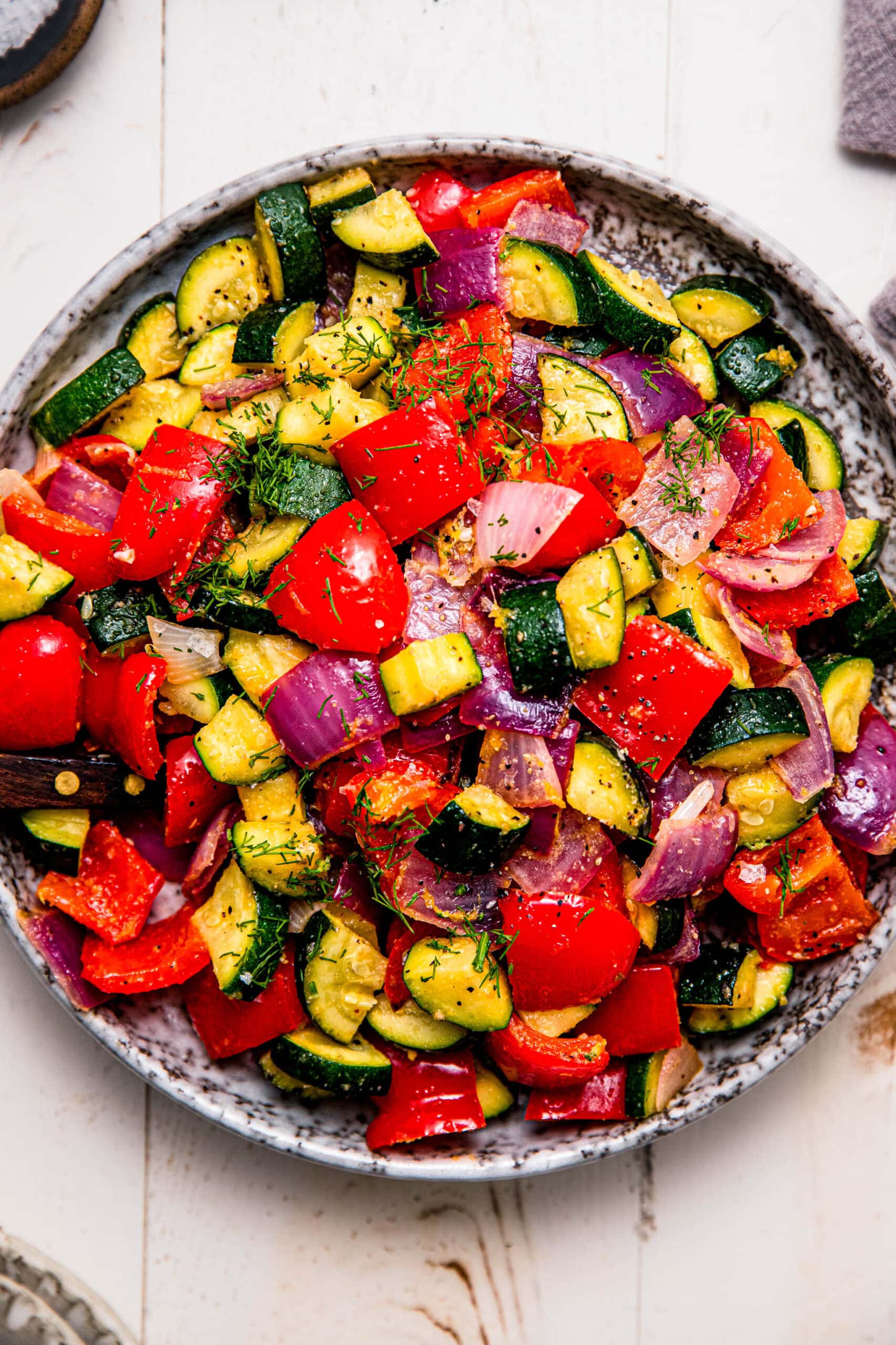 Overhead close up of serving plate of roasted zucchini and red peppers with red onion.