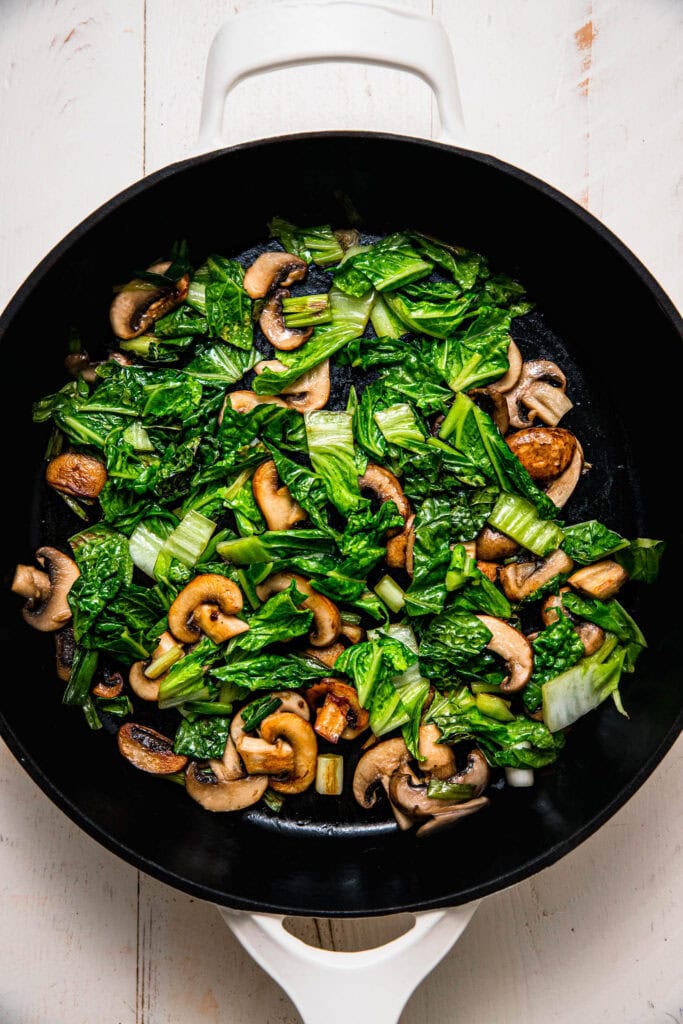 Cabbage and mushrooms being sauteed in wok. 
