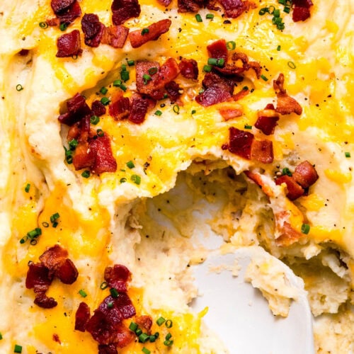 Spoon dipping into casserole dish of twice baked mashed potatoes topped with bacon & cheese.