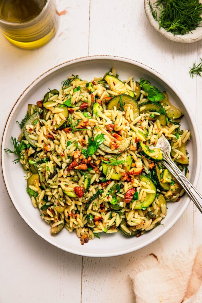 Zucchini orzo pasta salad in serving bowl on white counter.