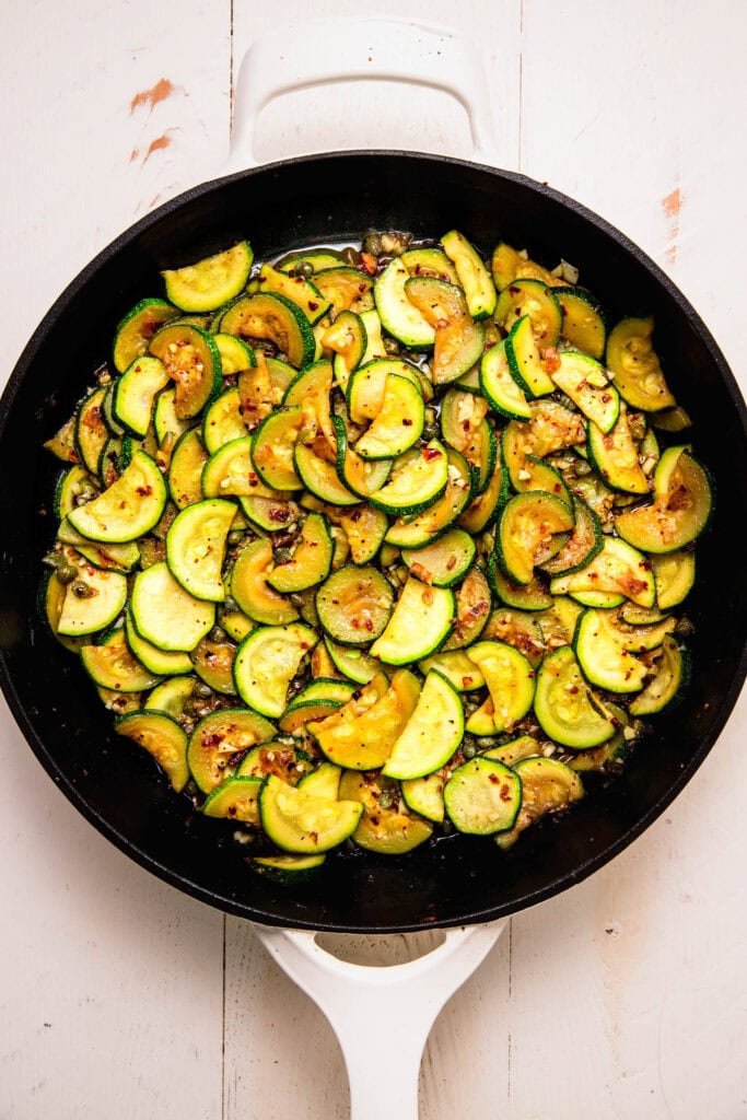 Sliced zucchini cooking in skillet.